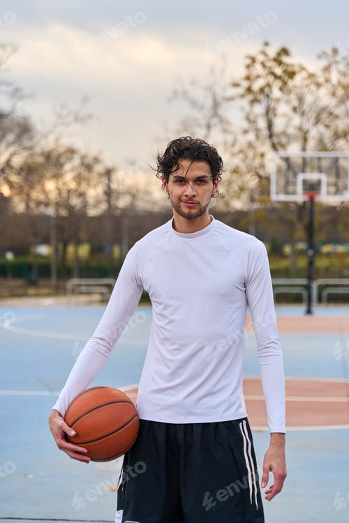 Preview: Young man holding basketball on urban court