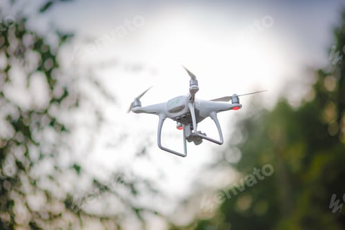 Preview: White flying quadrocopter with camera on green forest background