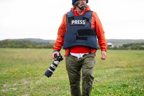 Preview: Reporter in bulletproof vest holding a camera.
