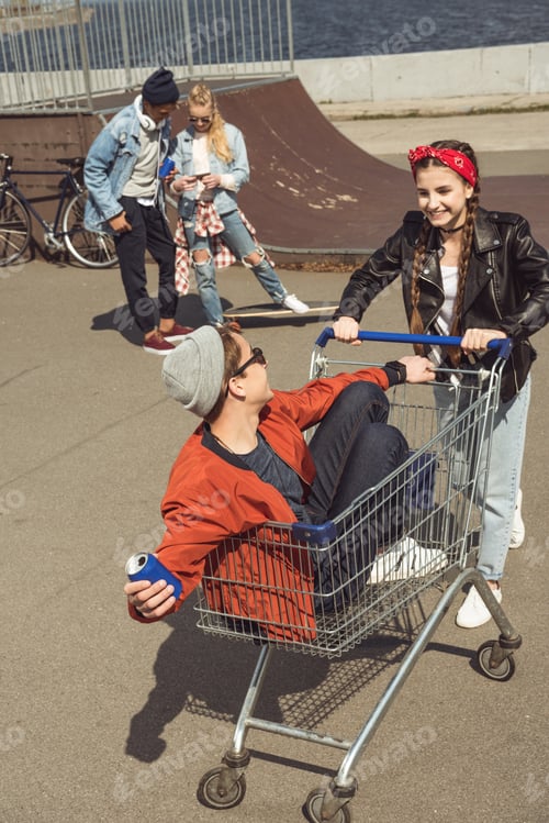 Preview: teenagers having fun with shopping cart in skateboard park, hipster style concept