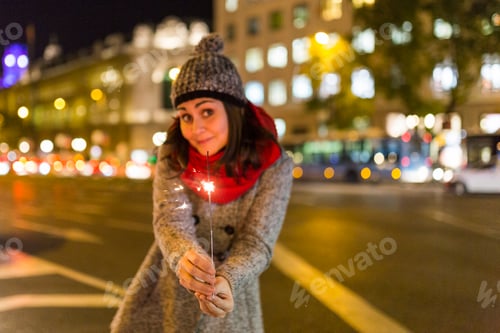Preview: beautiful young woman holding sparkle at night in city, having fun and smiling. Nightlife. Christmas