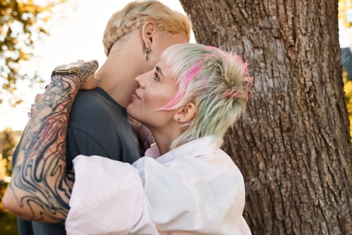 Preview: Young couple sharing a tender moment under a tree in a sunny park