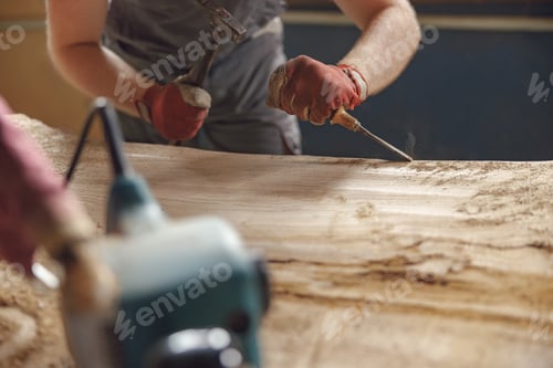 Preview: Close up of craftsman working with chisel while cutting wooden plank in carpentry workshop