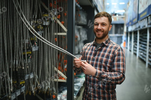 Preview: Portrait of a handsome workman choosing water pipes and pipe joints standing near the showcase