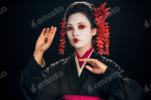 Preview: beautiful geisha in black and red kimono and flowers in hair gesturing isolated on black