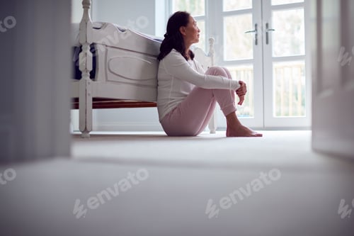 Preview: Unhappy And Depressed Mature Asian Woman In Pyjamas Sitting On Bedroom Floor