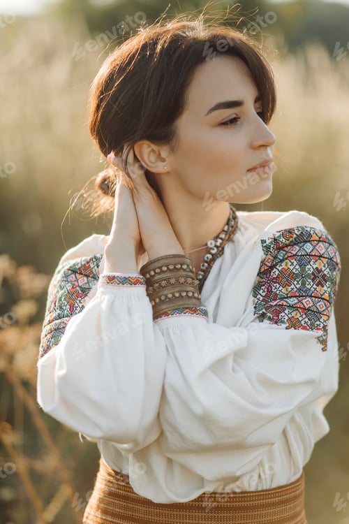 Preview: Young woman in traditional national embroidered shirt and skirt on nature at sunset.