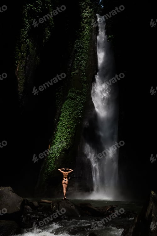 Preview: Beautiful young woman in bikini relaxing in front of waterfall. Ecotourism concept image travel girl