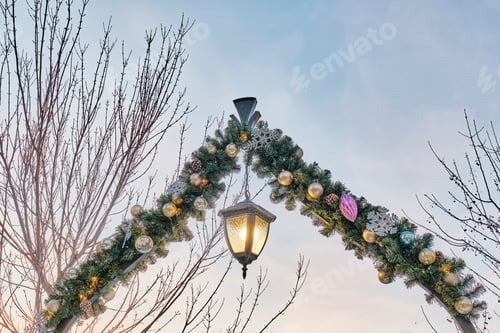 Preview: Christmas street arched decoration - coniferous garland with toys and a hanging lantern.