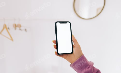 Preview: Young woman in using smartphone with white screen mock-up in white wardrobe room with floor rack.
