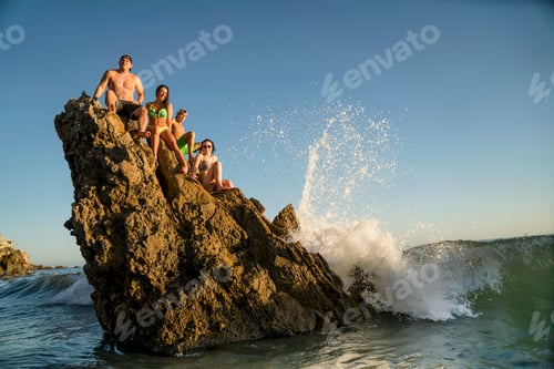 Preview: Adult friends sitting on rock formation at Newport Beach, California, USA