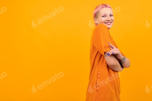 Preview: Unusual pretty woman with short pink hair and tattoo smiles isolated on orange background