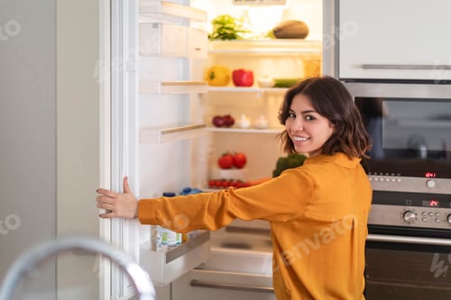 Preview: Portrait Of Happy Young Arab Woman Opening Fridge In Kitchen