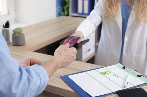 Preview: Receptionist taking payment from patient via terminal at counter in clinic, closeup