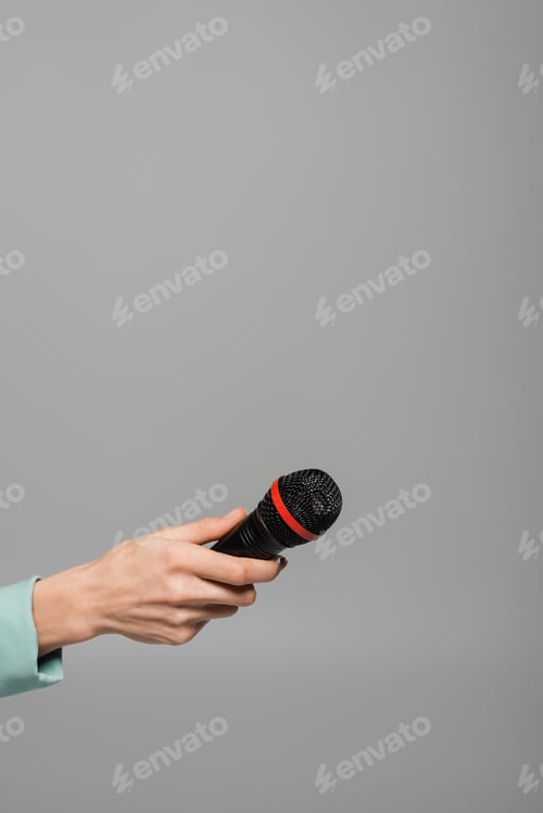 Preview: Cropped view of black wireless microphone in hand of event host in green jacket during performance
