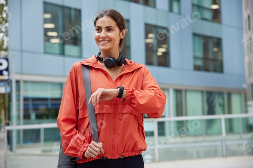 Preview: Waist up shot of happy brunette sporty woman dressed in anorak checks fitness results on smartwatch