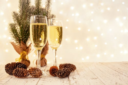Preview: glasses of champagne on a wooden table. The background with a blurred golden garland, sideways