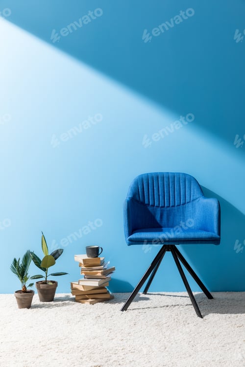 Preview: armchair with books and ficus pots in front of blue wall
