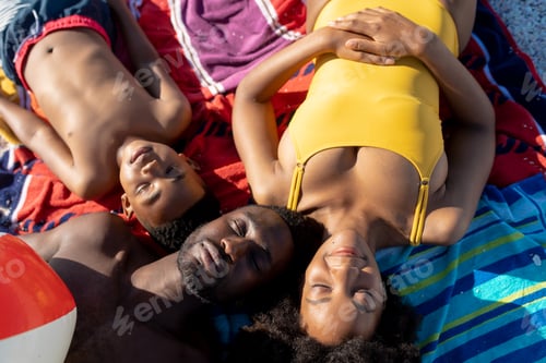 Preview: Directly above view of african american parents sleeping by son on beach towel during summer holiday