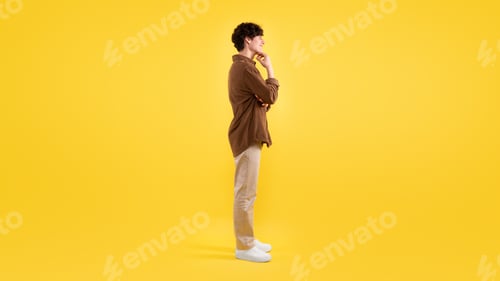 Preview: Smiling Young Man Touching Chin Looking Aside Over Yellow Background