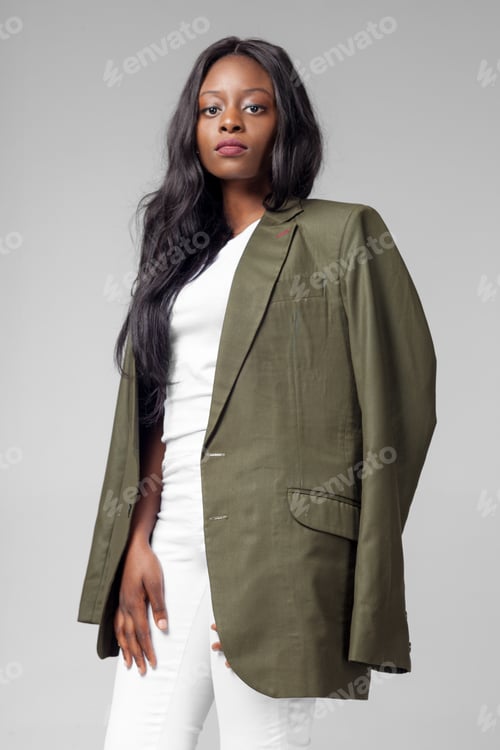 Preview: Woman in oversized blazer stands confidently with a serious expression against a plain background