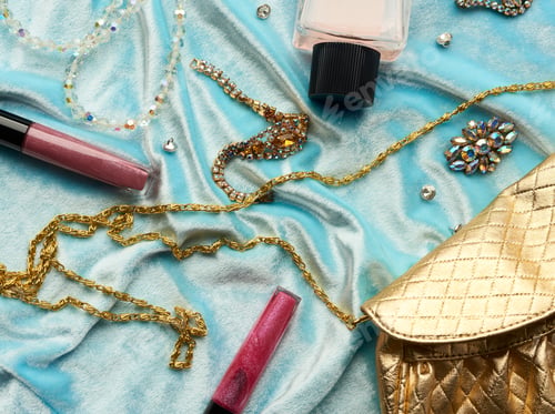Preview: Golden handbag, lip gloss and beads on a blue background