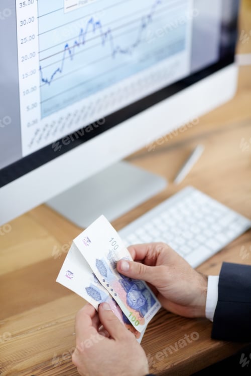 Preview: Cropped shot of a businessman counting money in front of a computer