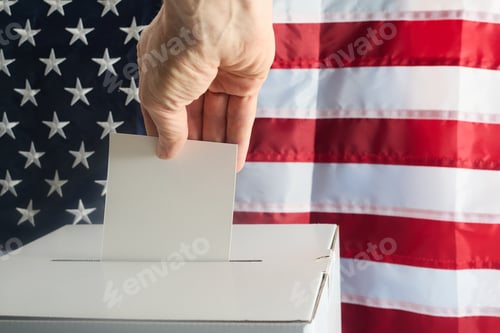 Preview: Hand putting his vote into ballot box against national flag of United States