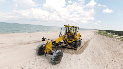Preview: Yellow tractor. Shot . A large tractor working on the ocean shore, which drives at speed and rakes