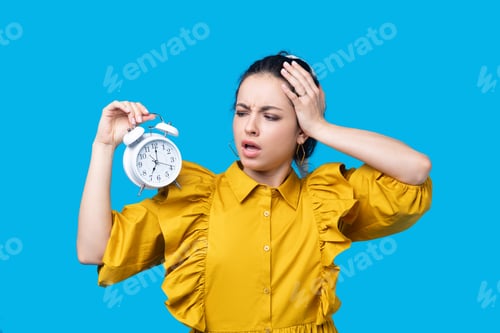 Preview: Woman in a mustard dress holding a clock and looking desperate