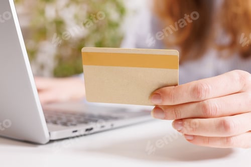 Visualização: Vista de perto da mão da mulher segurando um cartão de crédito, smartphone e usando o laptop