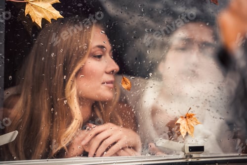 Preview: Young happy lovers couple behind wet misted window,rain drops.Drawing heart with finger.Autumn atmos