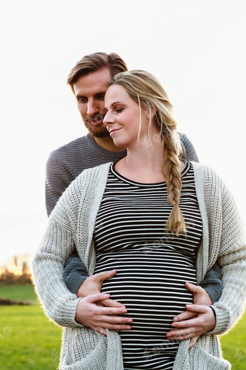 Preview: Man hugging and touching girlfriend's pregnant stomach in field landscape