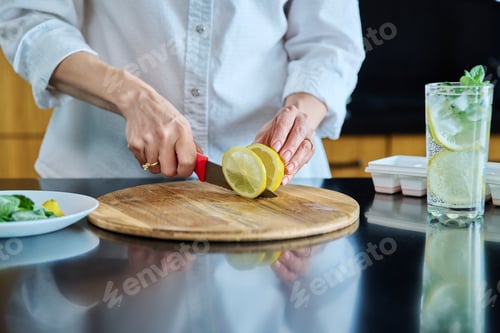 Preview: Closeup of a woman's hands preparing cold cocktail with lemon, mint leaves and ice