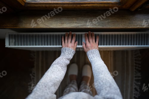 Preview: Woman in woolen sweater tries to catch stream of warm air from central heater touching device