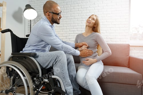 Preview: Disabled african american man touching the belly of his pregnant caucasian wife while they relax