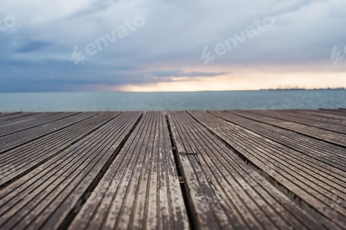 Preview: View of wooden decking, sea and gray sky at dusk.