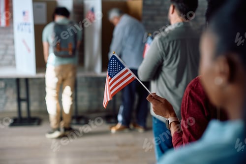 Preview: Close up of black voter with national flag in waiting line during US elections.
