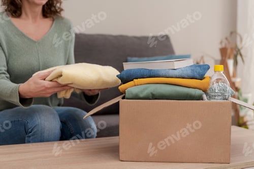 Preview: Close up of Woman sitting on sofa and preparing donation box with clothes and items