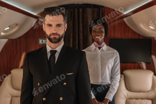 Preview: selective focus of confident pilot and smiling african american stewardess looking at camera in