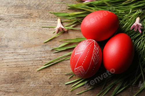 Preview: Flat lay composition of painted red Easter eggs and green grass on wooden table, space for text