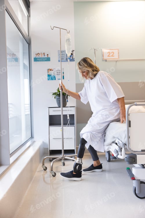 Preview: Senior caucasian female patient with prosthetic leg sitting on bed at hospital