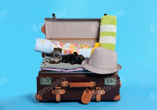 Preview: Open vintage suitcase with clothes packed for summer vacation on light blue background