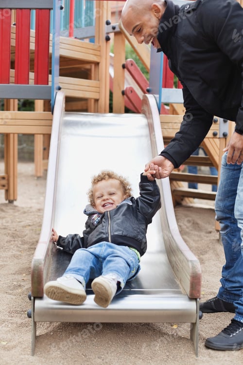 Preview: Happy father assisting son on slide at playground