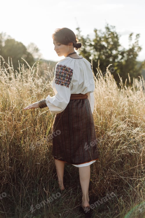 Preview: Young woman in traditional national embroidered shirt and skirt on nature at sunset.