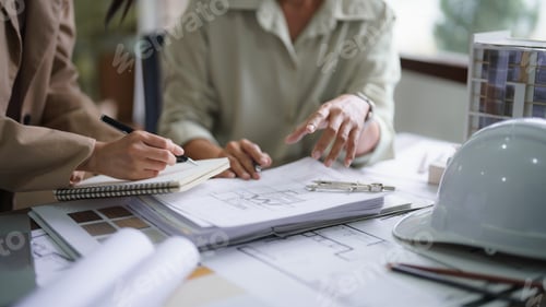 Preview: Two female architects discuss about interior design building project on blueprint and taking notes
