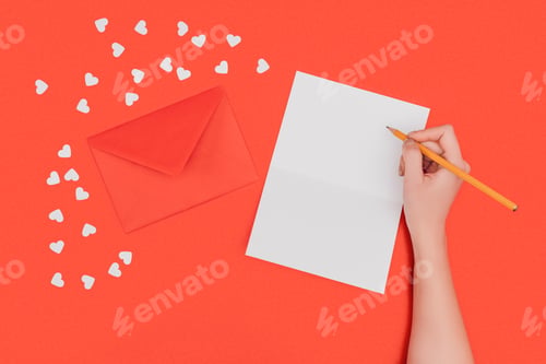Preview: cropped shot of person writing in white card, red envelope and small hearts isolated on red