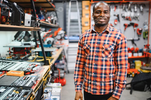 Preview: Confident smiling salesman on foreground in power tools store.