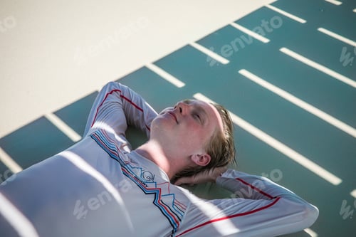 Preview: Young man lying in the sand on a beach underneath a dock with light and shadows on his body