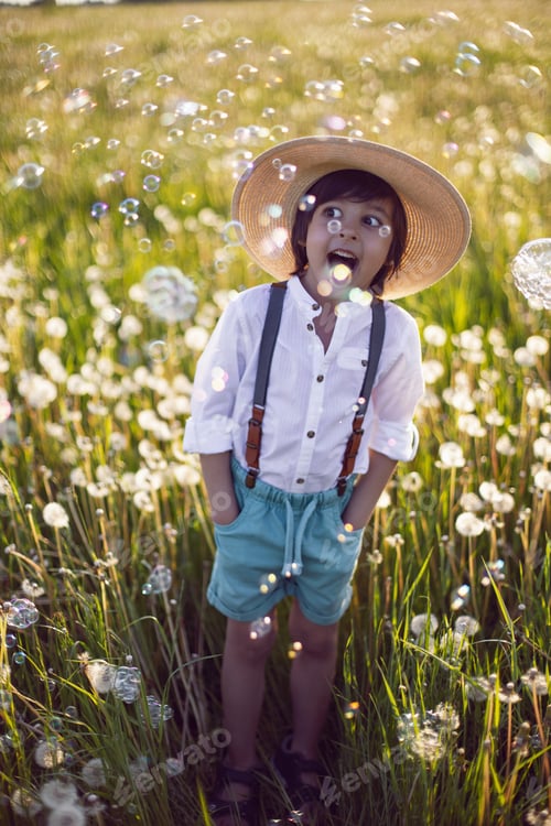 Preview: Portrait boy child in a field with dandelions at sunset. In a white shirt, hat and suspenders.